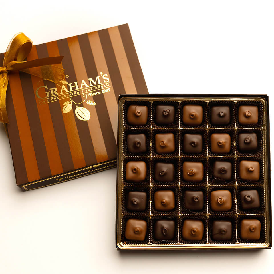 An open box of Graham's Gourmet Chocolates next to its striped brown and gold gift box with a gold ribbon, on a white background.