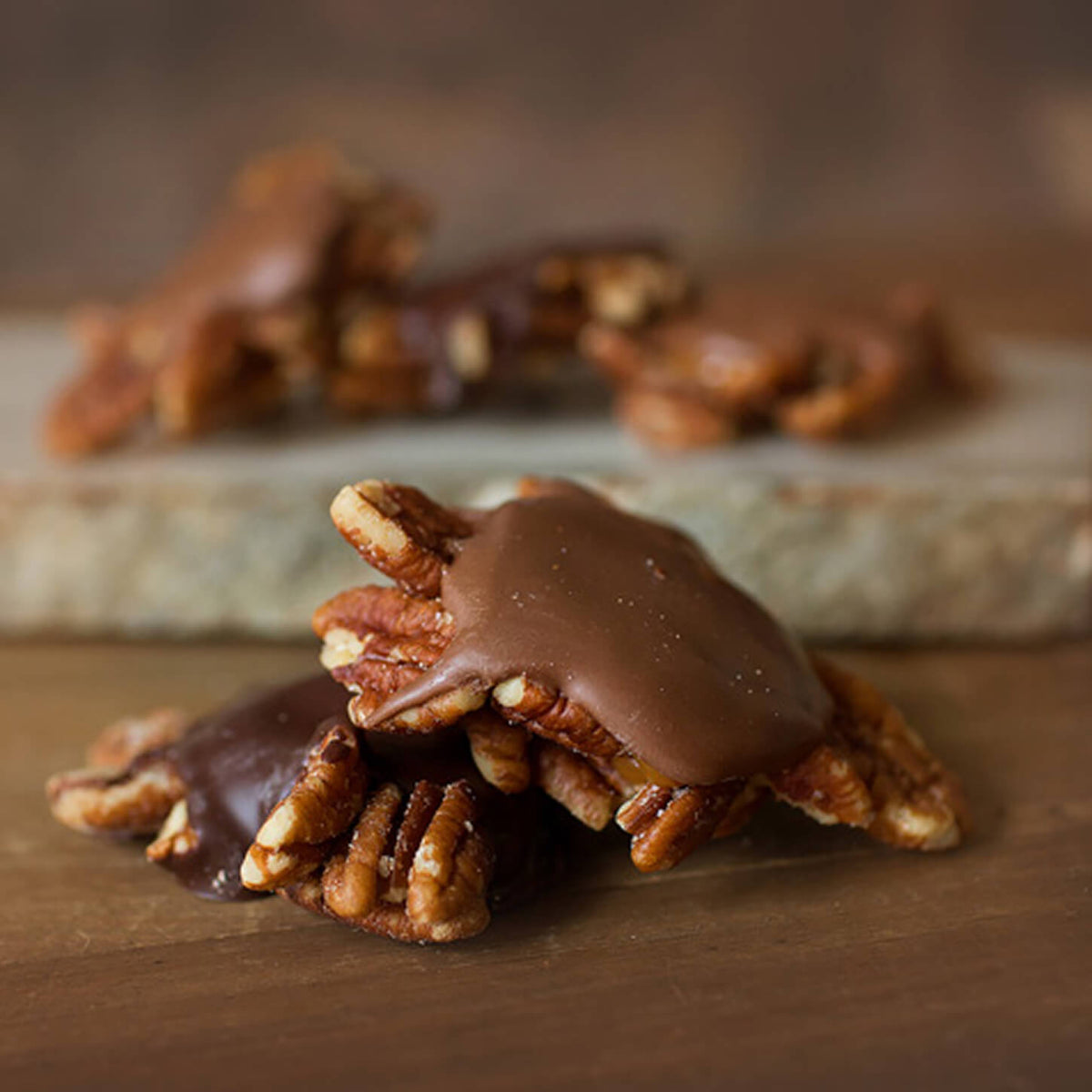 Chocolate-covered pecan clusters on a wooden surface with a blurred background.