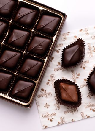 An open box of dark chocolate truffles and several individually wrapped chocolate pieces arranged on a white surface with a branded paper napkin. The brand name Grahams is visible on the napkin.
