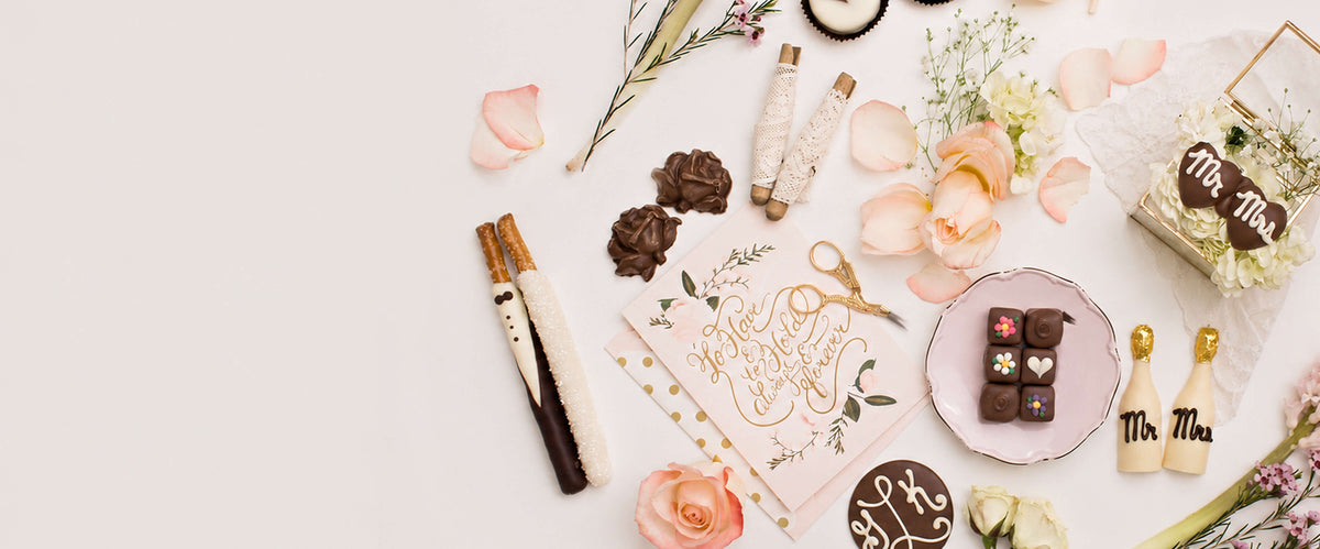 A styled flat-lay of wedding-themed stationery and chocolate treats on a white background, including a 'Mr. & Mrs.